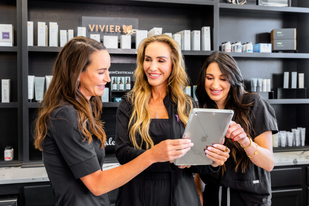 Three of our expert providers gather around an iPad, smiling, as they prepare to help clients at our weight loss clinic in Overland Park.
